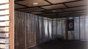 A spacious room with a wooden ceiling, dark wooden flooring, and a large window with blinds.