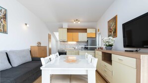 A modern kitchen with white cabinets, a dining table, and a flat-screen TV. - Green Hills Apartment (Dubrovnik)