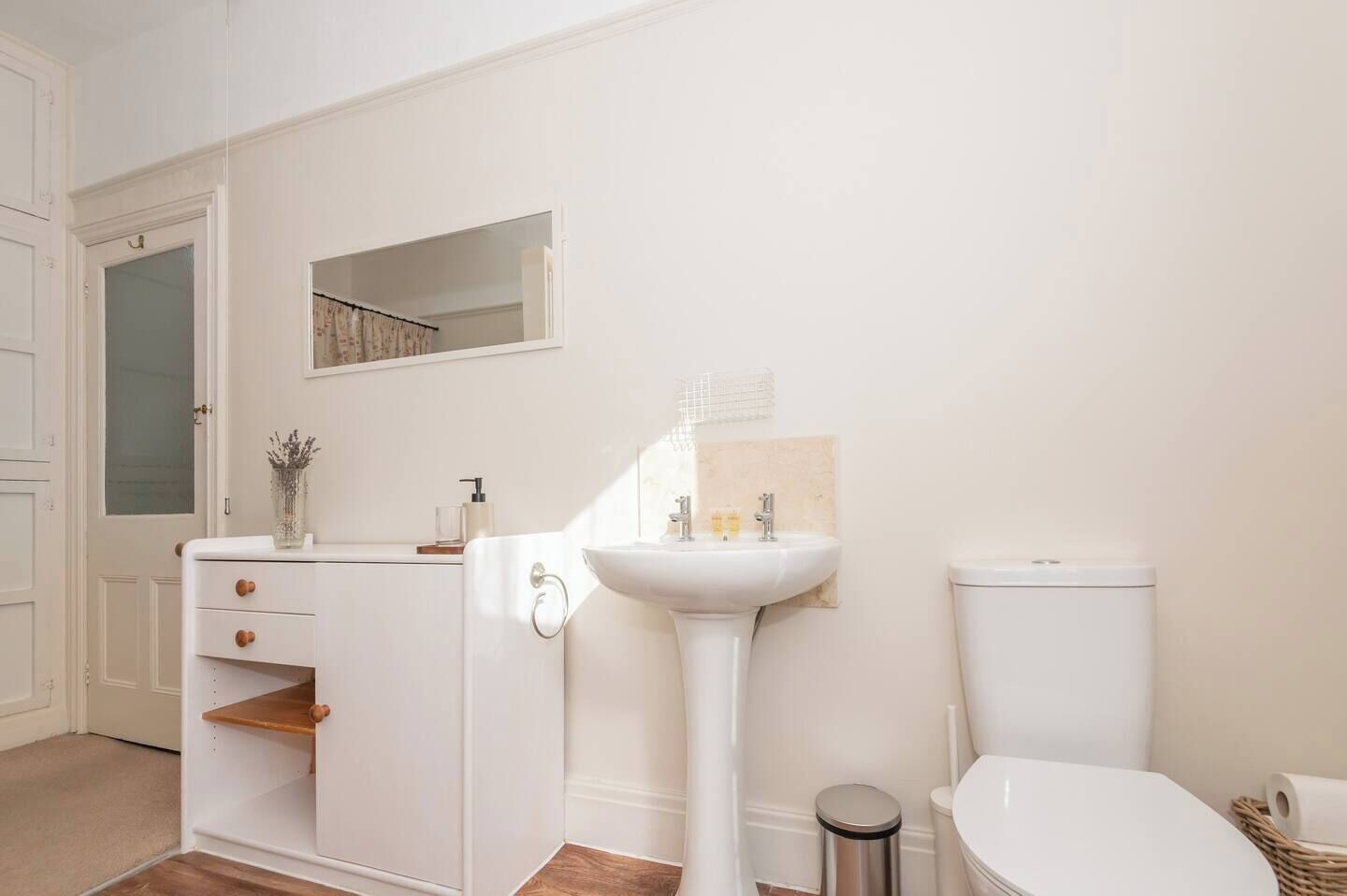 Une salle de bain avec un lavabo blanc, des toilettes et un meuble-lavabo doté de tiroirs et d’un miroir.