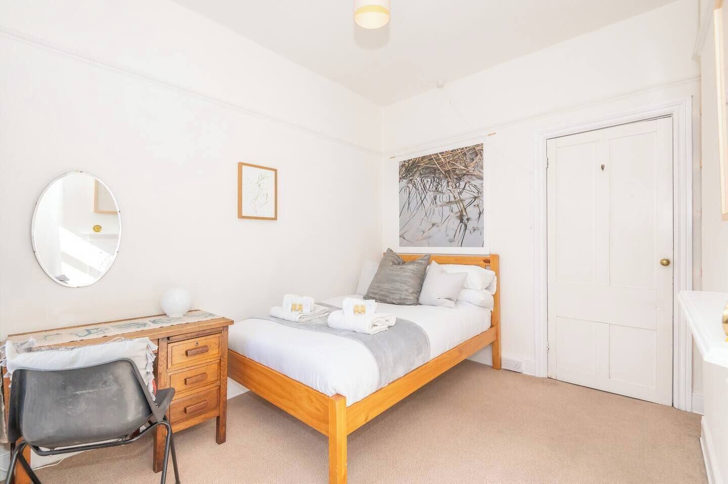 Un dormitorio con una cama de madera, un escritorio con silla, un espejo y una puerta.