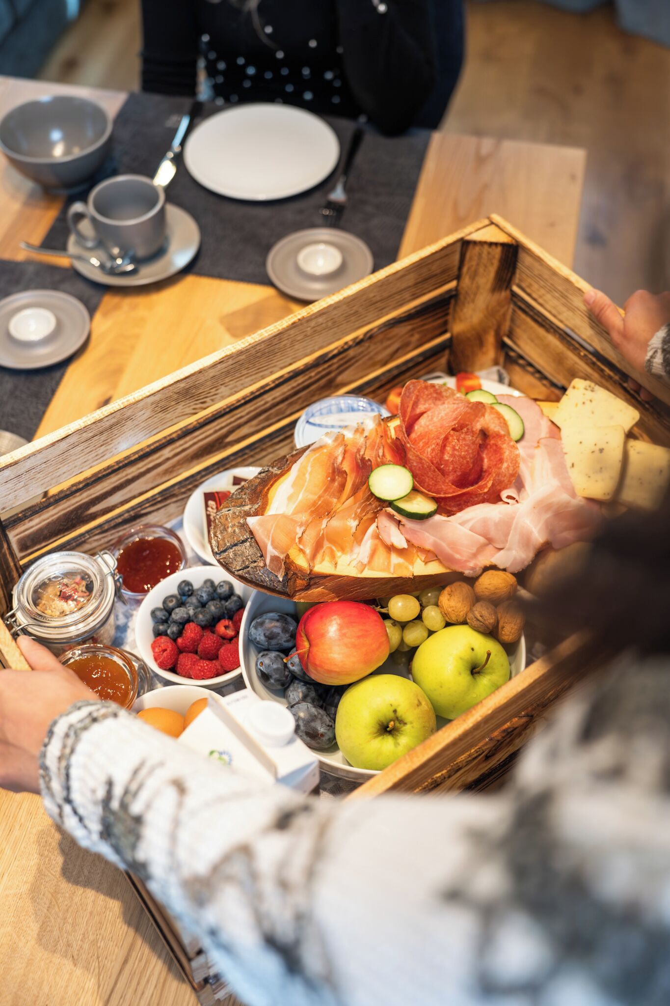 Ein Holztablett mit verschiedenen Speisen, darunter Obst, Käse und Fleisch.
