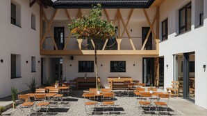 An outdoor seating area with wooden tables and chairs, surrounded by a building with a modern architectural design. - Rienz Apartment – Farm Stay in Nature and Relaxation (Naz-Sciaves)