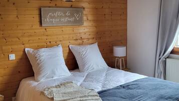 Une chambre à coucher avec une tête de lit en bois, un lit avec une literie blanche, un panneau décoratif, une petite table avec une lampe et une fenêtre avec des rideaux.