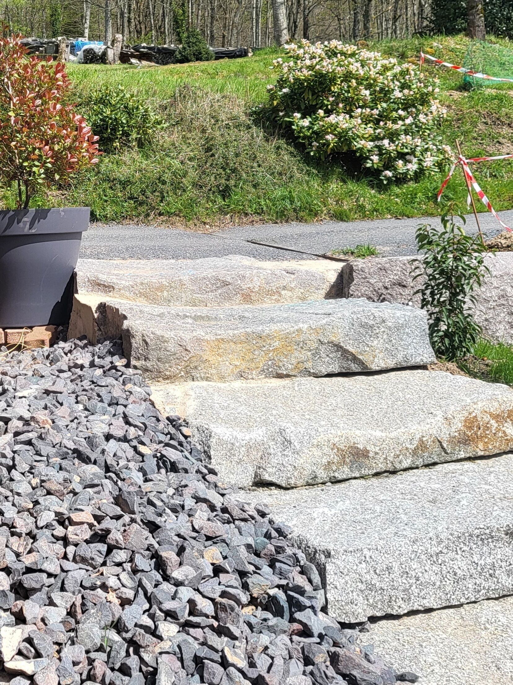 A stone pathway leading through a landscaped area with a large planter and a bush with white flowers.