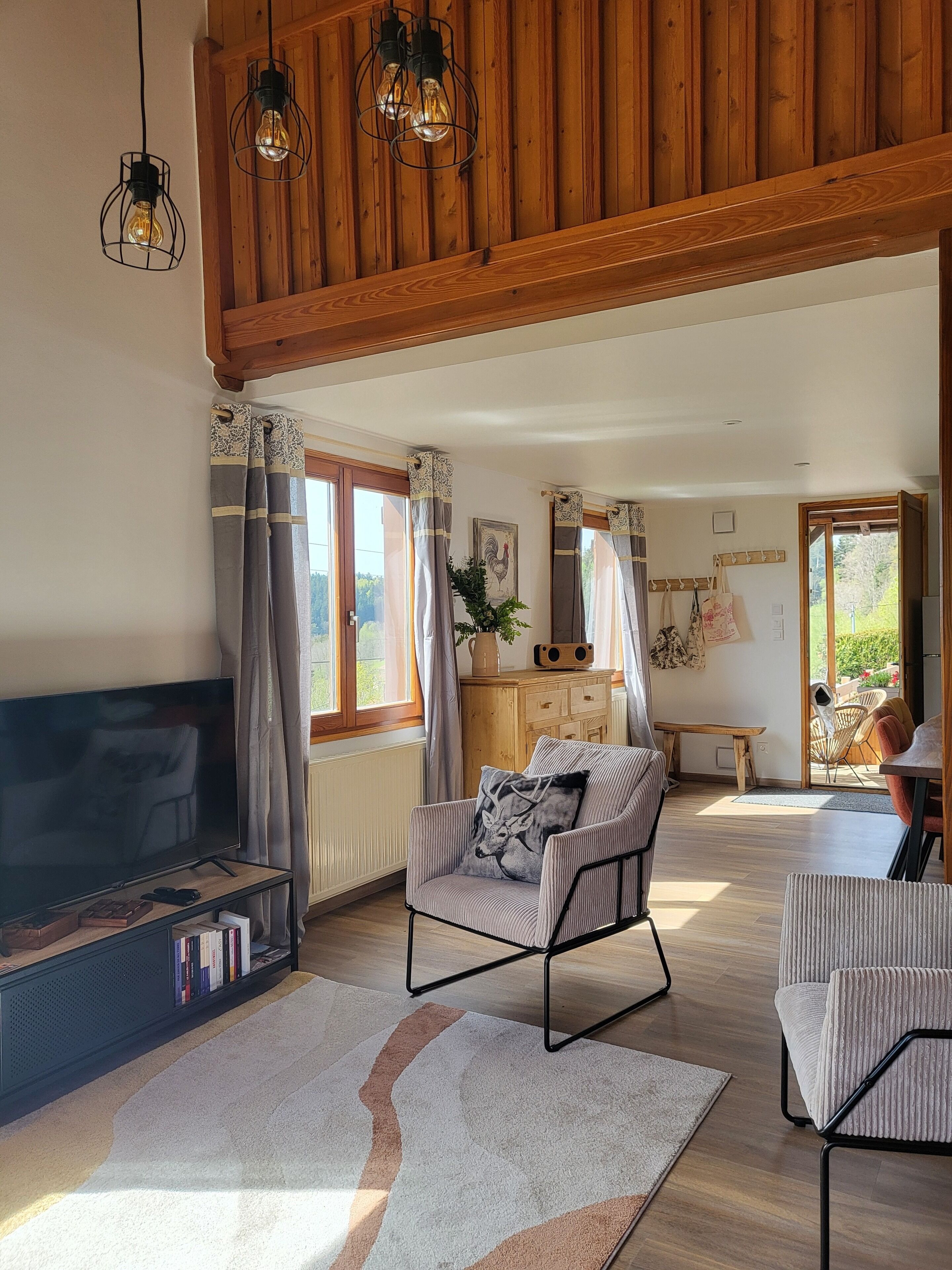 Un salon spacieux avec un plafond en bois, un grand téléviseur à écran plat, un fauteuil confortable et un coin repas comprenant une table et des chaises.