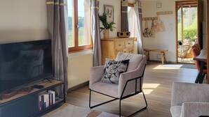 A spacious living room with a wooden ceiling, a large flat-screen TV, a comfortable armchair, and a dining area with a table and chairs. - L'évasion au Chalet de Fraize Avec vue Imprenable,équipé de Vélos Électriques (Fraize)