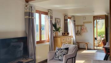 Un salon spacieux avec un plafond en bois, un grand téléviseur à écran plat, un fauteuil confortable et un coin repas comprenant une table et des chaises.