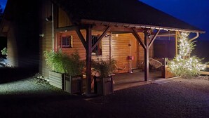 A wooden cabin with a covered porch, a small garden, and decorative lights. - L'évasion au Chalet de Fraize Avec vue Imprenable,équipé de Vélos Électriques (Fraize)