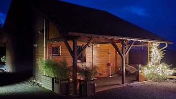 Une cabane en bois dotée d’un porche couvert, d’un petit jardin et de guirlandes lumineuses décoratives.