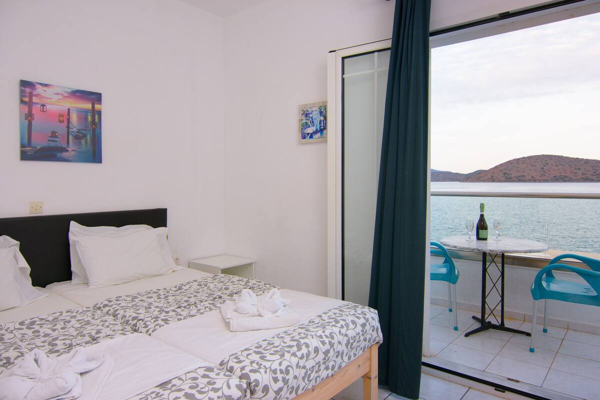 Habitació d'hotel amb un llit, una taula petita amb cadires, una ampolla de vi i vista al mar.