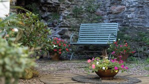 Un mur de pierre, un banc et des plantes en pot dans une cour.