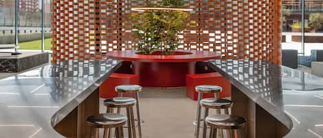 Um interior moderno com uma mesa redonda central rodeada por bancos, uma planta decorativa e uma parede com padrão.
