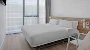 A modern hotel room with a large bed, a wooden headboard, a white chair, and a large window with sheer curtains. - B&B Hotel Porto Gaia (Vila Nova de Gaia)