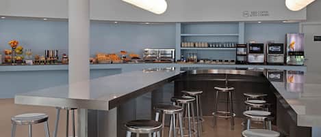 Un'area bar moderna con un lungo bancone, diversi sgabelli e una selezione di bevande e snack.
