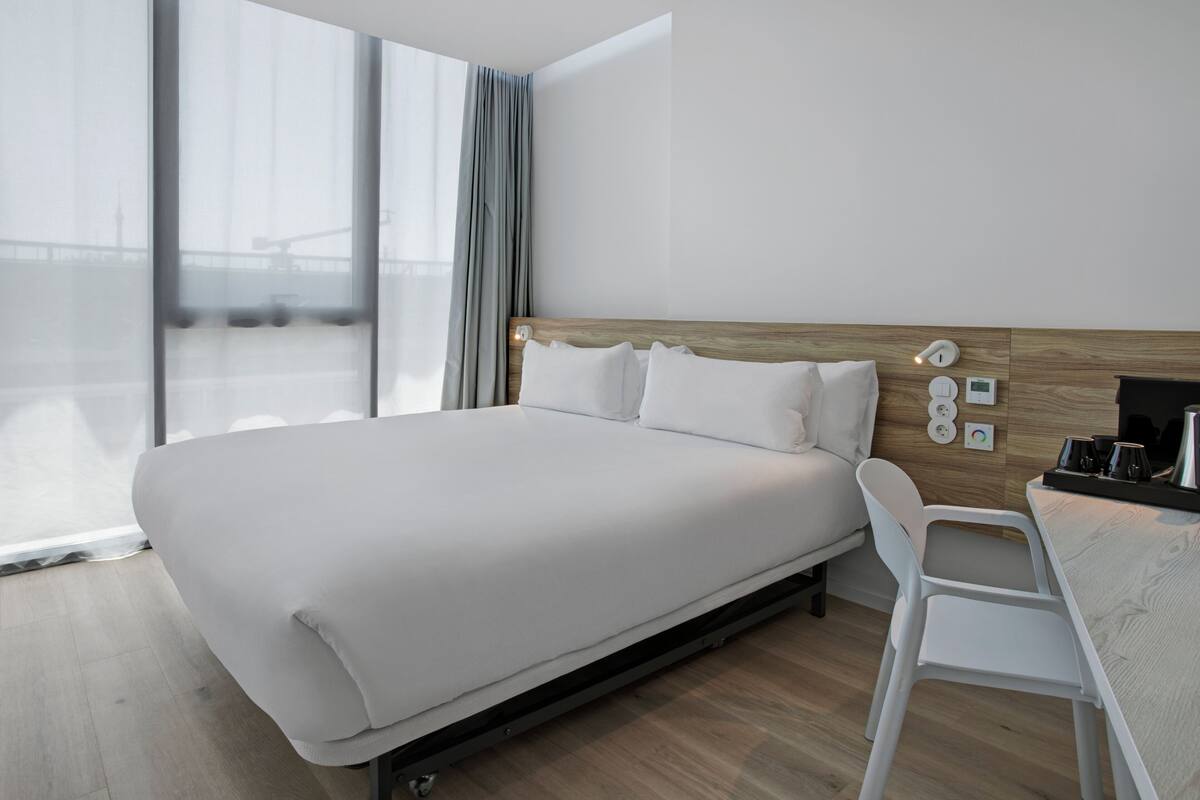 A modern hotel room with a large bed, a desk, and a view of the city.