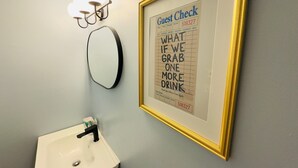 Un cadre contenant un reçu de client agrémenté d’une note humoristique, un miroir fixé au mur et un lavabo avec un robinet.