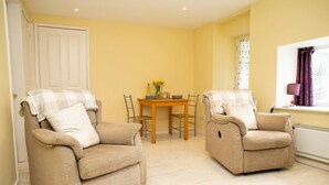 A room with two beige armchairs, a wooden dining table with chairs, a window with purple curtains, and a radiator. - Penlon Annex, Aberporth (Aberporth)