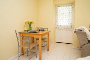 A small dining area with a wooden table and metal chairs, a vase with yellow flowers, a bottle of white wine, and a glass.