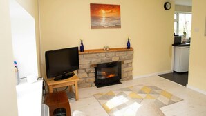 A living room with a fireplace, a television on a stand, and a painting of a sunset. - Penlon Annex, Aberporth (Aberporth)