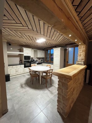 Une cuisine avec un îlot central en pierre, un plafond en bois et des armoires blanches.
