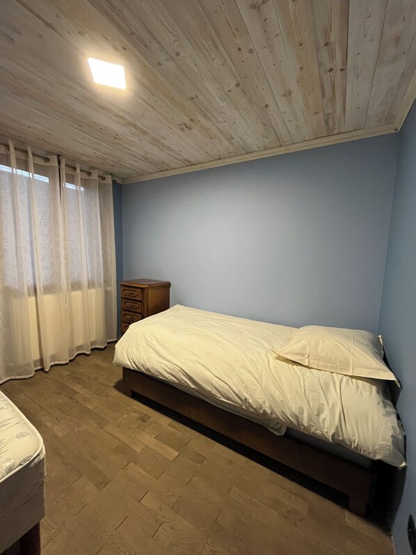 Une chambre à coucher avec un lit en bois, une table de chevet et une fenêtre avec des rideaux.