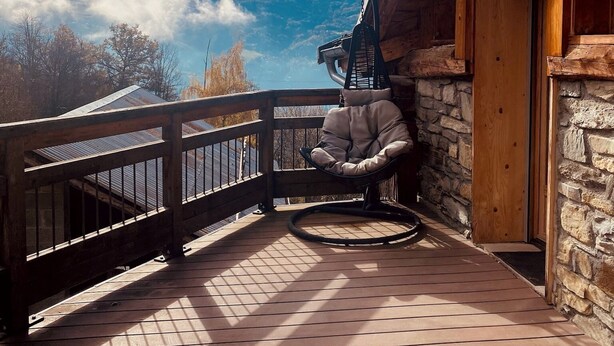 Una terraza de madera con un muro de piedra y una silla, con vistas a una cordillera.