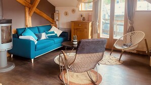 Una sala de estar acogedora con un sofá azul, sillones de mimbre, una chimenea y un ventanal grande.