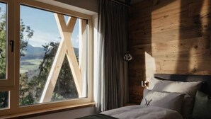 Ein Schlafzimmer mit Holzkopfende, einem großen Fenster mit Blick ins Freie und einem Bett mit Kissen.