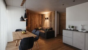 Eine moderne Küche mit Holzschränken, ein Essbereich mit Holztisch und -stühlen sowie eine gemütliche Sitzecke mit Sofa und Kissen.