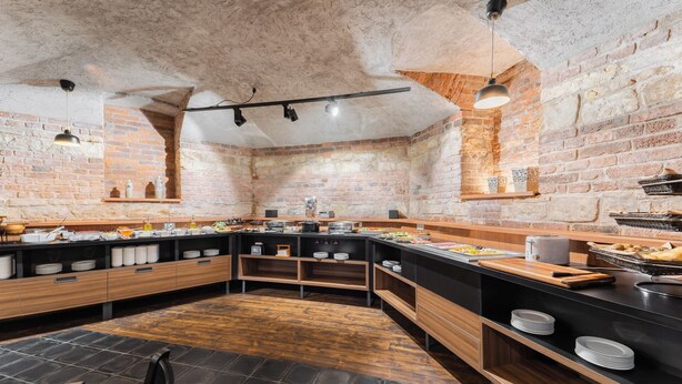 A modern kitchen with a brick wall, wooden cabinets, and a black countertop. - EA Hotel Victoria (Prague)