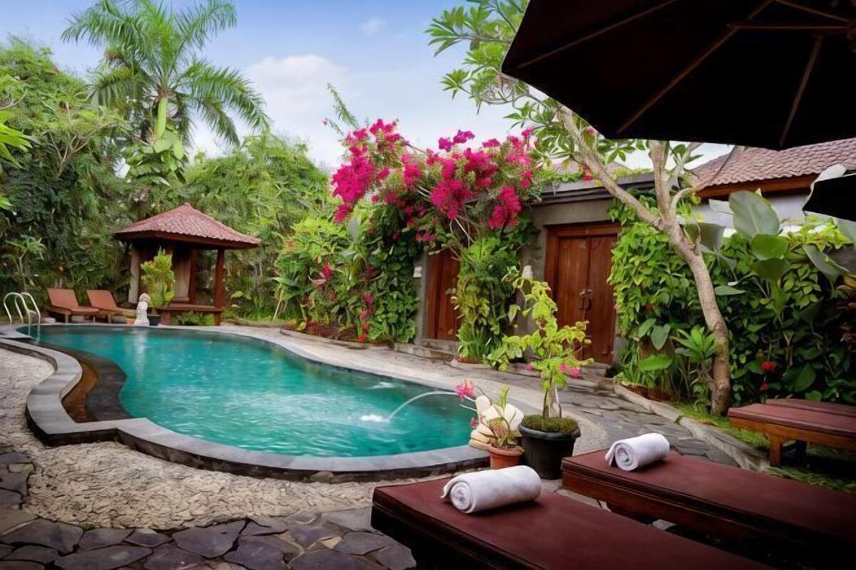 A swimming pool surrounded by lush greenery, a wooden deck, and a small gazebo.