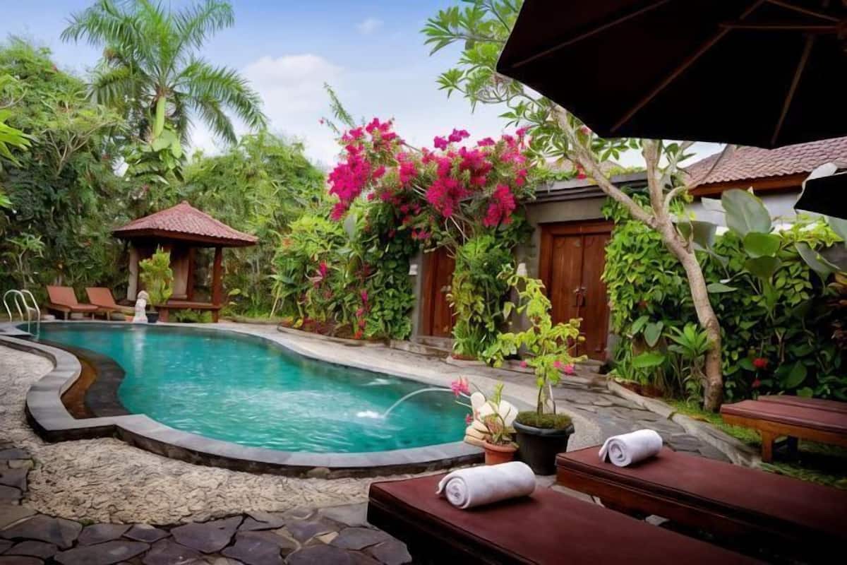 A swimming pool surrounded by lush greenery, a wooden deck, and a small gazebo.
