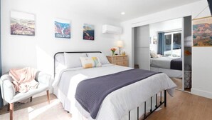 A bedroom with a bed, bedside table, lamp, and a chair. There are posters on the wall and a sliding door leading to another room. - Downtown Mammoth | Walk to Shops & Eats! MH#5 (Mammoth Lakes)