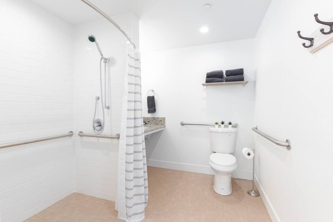 A bathroom with a shower, toilet, grab bars, and a towel rack.
