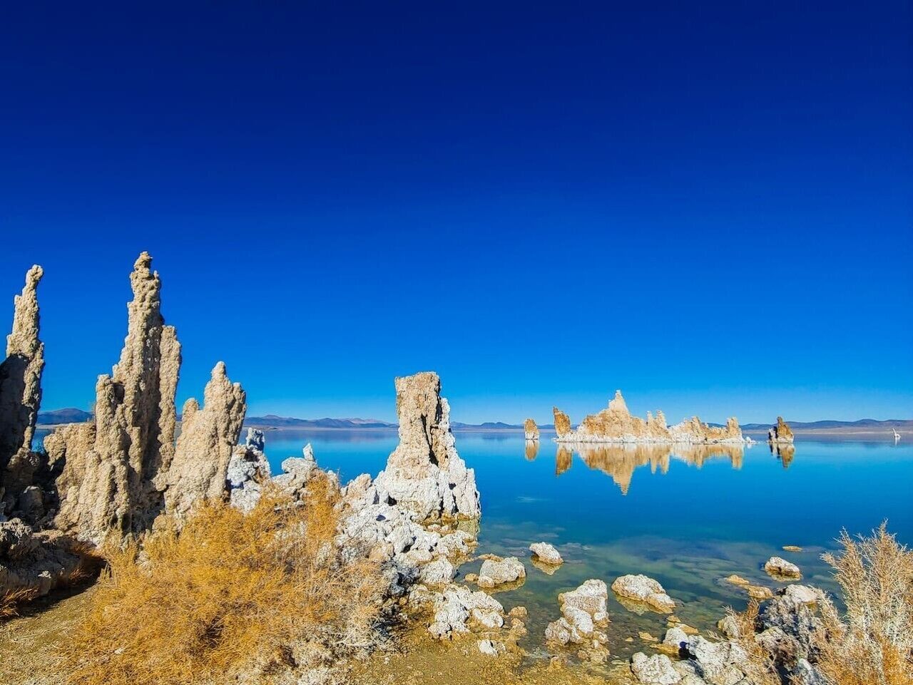 Un lac aux eaux limpides, bordé de formations rocheuses, et un ciel d’un bleu éclatant.