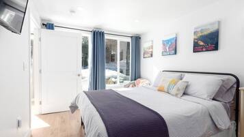 A bedroom with a bed, a window with curtains, a door, and a wall-mounted TV.
