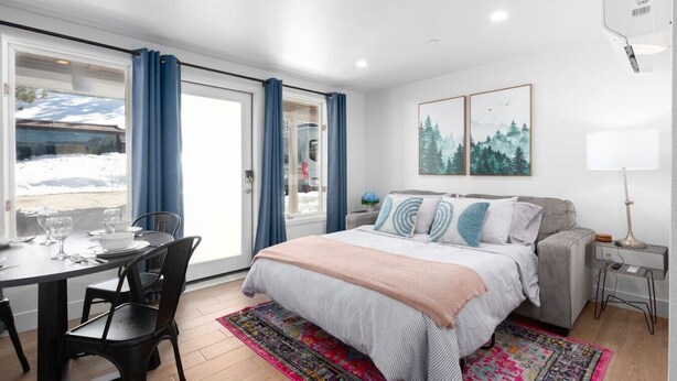 A hotel room with a bed, a dining table with chairs, a window with curtains, a bedside table with a lamp, and two framed pictures on the wall. - New! Near Restaurants and Shopping #6 (Mammoth Lakes)
