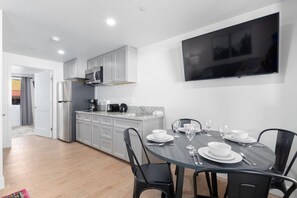 A modern kitchen with grey cabinets, a stainless steel refrigerator, a microwave, and a flat-screen TV mounted on the wall.
