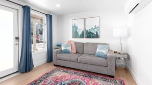 A living room with a grey sofa, a colorful rug, two framed pictures, a lamp, and a window with curtains. - New! Near Restaurants and Shopping #6 (Mammoth Lakes)