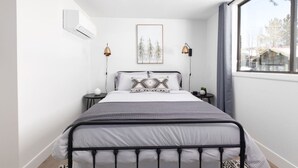 A bedroom with a bed, a window, a wall-mounted air conditioner, and a framed picture.