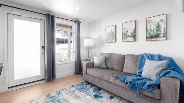 A living room with a grey sofa, a blue blanket, a lamp, and framed pictures on the wall.