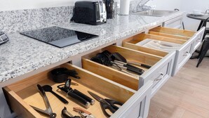 A kitchen with a granite countertop, a toaster, a kettle, and a tablet. There are wooden drawers below with various kitchen utensils.