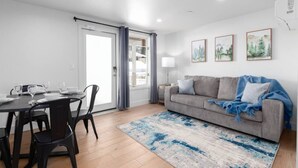 A modern living room with a dining area, a grey sofa, a blue throw blanket, and framed pictures on the wall.