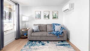 A modern living room with a grey sofa, a lamp, and framed pictures on the wall.