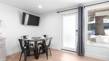 A dining area with a table set for four, a flat-screen TV mounted on the wall, and a sliding glass door leading to a snowy outdoor area.