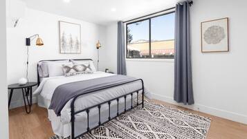 Een moderne slaapkamer met een groot raam, een bed met een bedsprei met dessin, en twee wandlampen.