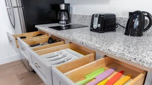 Eine Küche mit einer Granitabdeckung, einer Kaffeemaschine, einem Toaster und einem Wasserkocher. Es gibt mehrere Schubladen mit Kochgeschirr und bunten Besteck.