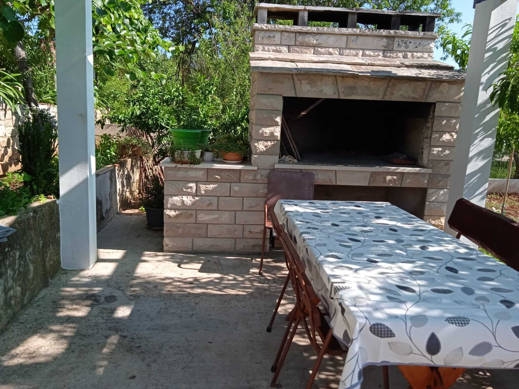 Un patio al aire libre con zona de barbacoa de piedra, una mesa con mantel estampado y plantas en macetas.
