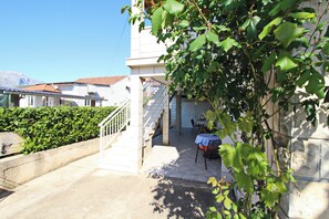 A courtyard with a staircase leading to a covered area, surrounded by greenery and a stone wall. - Apartments Marita (Korcula)