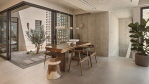 A modern dining area with a wooden table and chairs, a potted plant, and a view of the outside. - Villa Albero: Your Stay, a Seaview Journey (Souda)